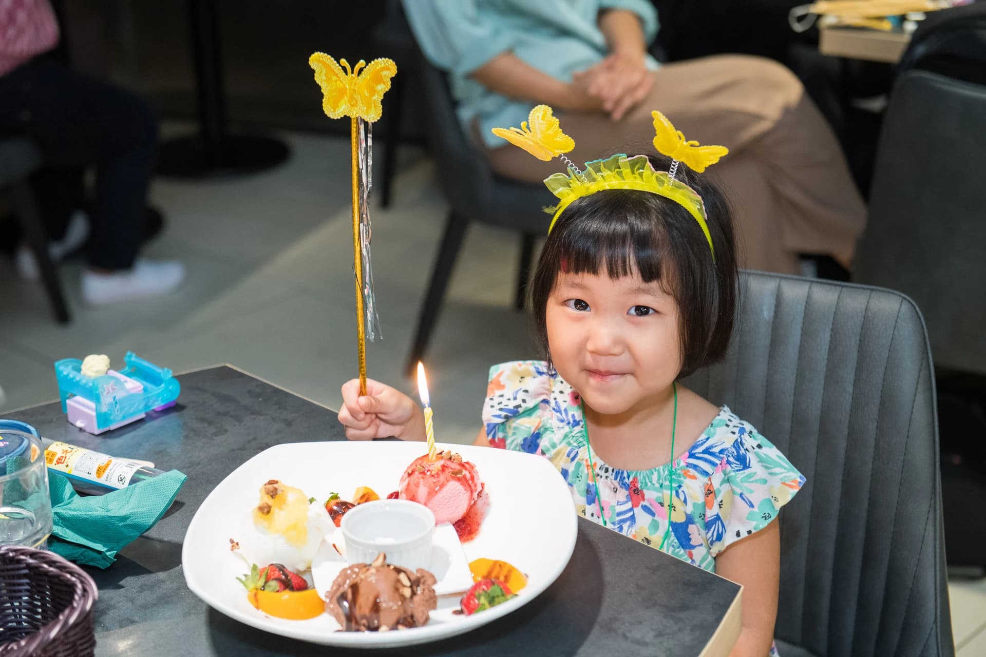 A child smiling beside an ice-cream dessert with a birthday candle